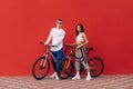 Young couple man and woman posing with bicycles on red background, wearing stylish sportswear. Couple ride a bike Royalty Free Stock Photo