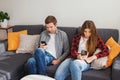 Young couple, man and woman using their mobile phones while sitting on the couch Royalty Free Stock Photo