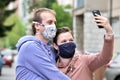 Young couple, man and woman, wearing DIY facemasks and taking a selfie in the street.