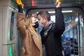 Young couple in medical masks holding handrails in subway car.