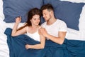 Bedtime. Young couple lying on bed under blanket top view hugging waking up cheerful Royalty Free Stock Photo