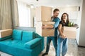 Young couple man and woman looking happy standing with boxes in their hands in new appartment unpacking boxes