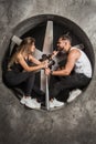 A young couple a man and a woman with a playful mood, fashionable and sporty look sit near an industrial fan in the factory with a