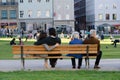 A young couple in the middle of a bench are putting their arms around each other and an old couple on the edge of the bench