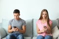 Young couple with mobile phones sitting on sofa at home Royalty Free Stock Photo