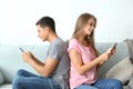 Young couple with mobile phones sitting on sofa at home Royalty Free Stock Photo
