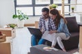 Young couple moving in new home. Sitting and relaxing after unpacking. Looking something on laptop