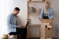 Young couple moving in new home. Happy homeowners sitting in a apartment using a laptop. A woman is unpacking things