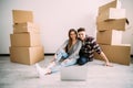 Young couple moving in new home sitting on floor and relaxing after unpacking looking something on laptop. Relocation Royalty Free Stock Photo