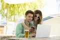 A young couple outdoors with a computer a beer and a phone and sunglasses. This is their lifestyle, cheerful love and work