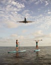 Young couple paddling on SUP board with landing Airplane