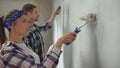 Young couple painting wall with white paint using paint rollers on window backdrop. Pretty woman and man in checkered Royalty Free Stock Photo