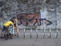 Young couple parking their bicycles in town at a bicycle rack in front of a graffiti wall