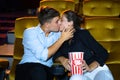 Young couple people kissing at movie theater. In hand holding snack bucket and throw popcorn around the seat Royalty Free Stock Photo