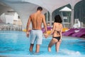 Young couple with perfect figure standing in the swimming pool and holding hands on luxury resort. Back view Royalty Free Stock Photo