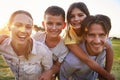 Young couple piggybacking their kids outdoors look to camera Royalty Free Stock Photo