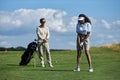 Young couple playing golf in green field with black woman hitting ball with club Royalty Free Stock Photo