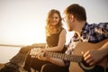 Young couple playing guitar sing a song together on countryside in nature park in morning with sunset outdoors in Royalty Free Stock Photo