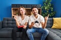 Young couple playing video game holding controller at home smiling happy pointing with hand and finger to the side Royalty Free Stock Photo