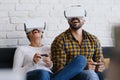 Young Couple Playing Virtual Reality With Headset On Sofa