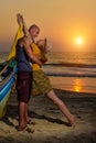 Young couple posing against sea at sunset. Guy and girl fooling and grimace near the old wooden boat on the ocean coast Royalty Free Stock Photo