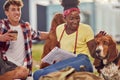 A young couple is posing for a photo while sitting on the grass in the park with their dogs. Friendship, rest, pets, picnic