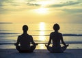 Young couple practicing yoga in the lotus position on the ocean beach during sunset. Royalty Free Stock Photo