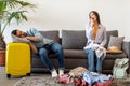 Young couple preparing for vacation, woman packing suitcases and yawning while husband sleeping on sofa Royalty Free Stock Photo