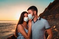 A young couple in protective masks posing on the sunset of the sea. In the background, the sea. The concept of travel during the Royalty Free Stock Photo