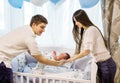 Young couple putting crying newborn son to sleep in white crib