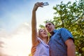 Young couple quaver and taking selfie in spring garden at sunset. Woman and man showing their toungues. Guys having fun.