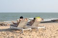 Young couple relaxing on the beach chair reading book and using cell phone.