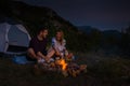 Young couple relaxing by the campfire and drinking coffee in the forest hill in the dusk