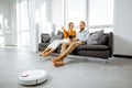 Young couple relaxing while automatic vacuum cleaner working at home