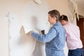 Young couple removing old wallpaper from walls preparing for flat renovation.