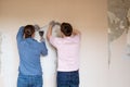 Young couple removing old wallpaper from walls preparing for flat renovation.