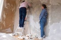 Young couple removing old wallpaper from walls preparing for flat renovation.