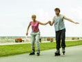 Young couple rollerblading in park holding hands. Royalty Free Stock Photo