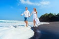 Young couple run by black sand beach along sea surf Royalty Free Stock Photo