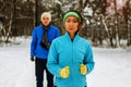 Young couple running dressed warmly in fleeces and gloves jogging in sunshine across winter snow