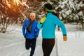 Young couple running dressed warmly in fleeces and gloves jogging in sunshine across winter snow