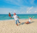 Young couple running at sea beach in santa hats with sled and christmas tree