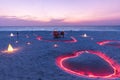 Beach sunset, anniversary couple table setting with candles and heart shape lights close to calm sea Royalty Free Stock Photo