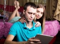 Young couple shopping online using digital tablet computer. Couple laughing, girl lying on the bed at home and guy Royalty Free Stock Photo