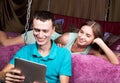 Young couple shopping online using digital tablet computer. Couple laughing, girl lying on the bed at home and guy Royalty Free Stock Photo