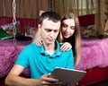 Young couple shopping online using digital tablet computer. Couple laughing, girl lying on the bed at home and guy Royalty Free Stock Photo