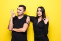 Young couple showing ok sign with and giving a thumb up gesture isolated over yellow background Royalty Free Stock Photo