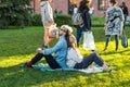 Young couple sit back to back on the lawn in the park with closed eyes and listen to music