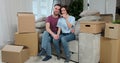 Young couple sit on sofa near cardboard boxes, wife showing to camera bunch of keys, new modern home. Couple move into