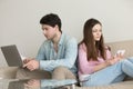 Young couple sitting back to back using laptop computer, tablet